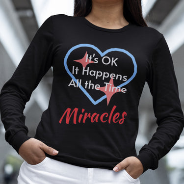 Long-sleeve Bella+Canvas t-shirt made from preshrunk ring-spun cotton with “Miracles Happen” design and message, “It’s OK. It Happens All the Time – Miracles,” faith-based apparel encouraging daily miracles through intimacy with God, woman wearing long-sleeve black t-shirt